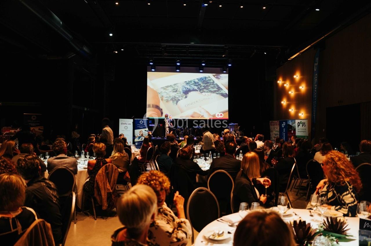 Salle de réception avec des invités assis, regardant une présentation projetée sur un écran.