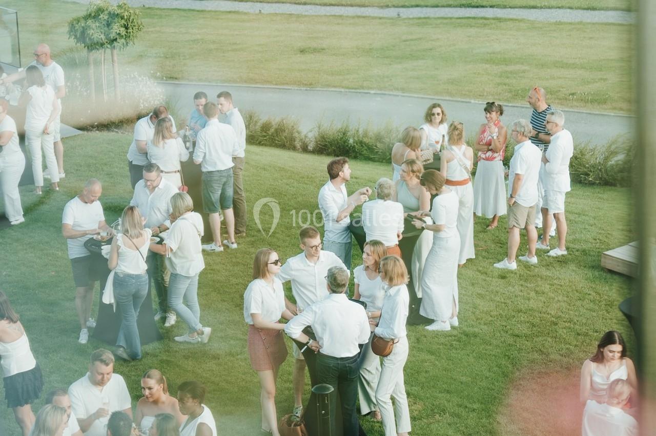 Groupe de personnes en tenue blanche discutant et partageant un moment convivial dans un jardin lors d'un événement en plein…
