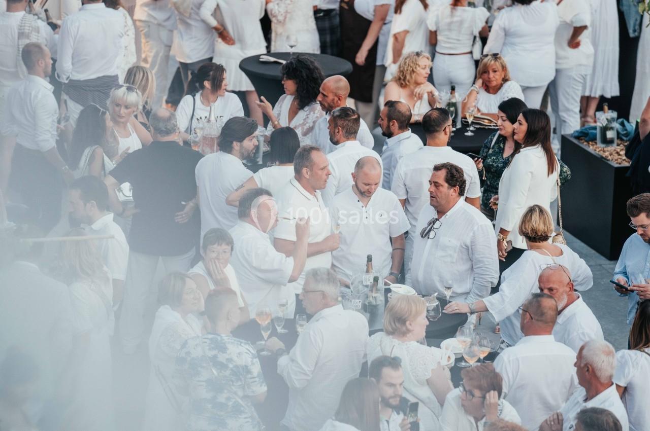 Groupe de personnes vêtues de blanc discutant et partageant un moment convivial lors d'un événement en plein air.