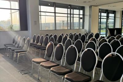 Rangées de chaises noires alignées dans une salle lumineuse avec une table en bois au premier plan.