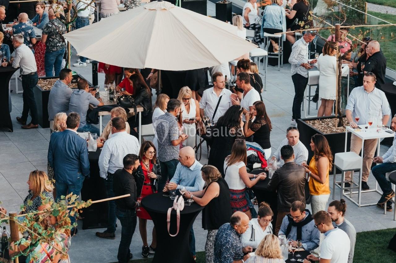 Groupe de personnes discutant et partageant un moment convivial lors d'un événement en plein air avec tables et parasols.