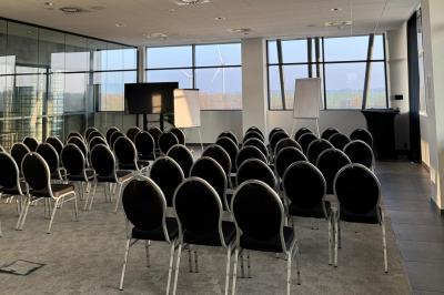 Rangées de chaises noires alignées dans une salle lumineuse avec une table en bois au premier plan.