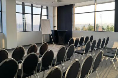 Rangées de chaises noires alignées dans une salle lumineuse avec une table en bois au premier plan.