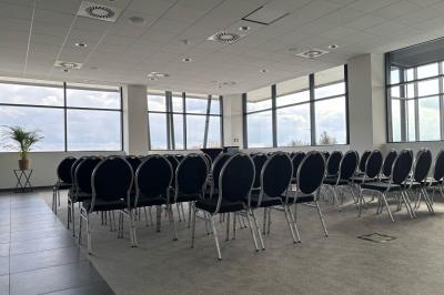 Rangées de chaises noires alignées dans une salle lumineuse avec une table en bois au premier plan.
