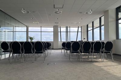 Rangées de chaises noires alignées dans une salle lumineuse avec une table en bois au premier plan.