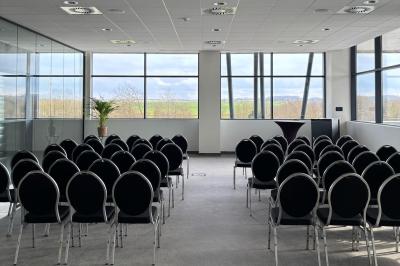 Rangées de chaises noires alignées dans une salle lumineuse avec une table en bois au premier plan.