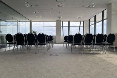Rangées de chaises noires alignées dans une salle lumineuse avec une table en bois au premier plan.