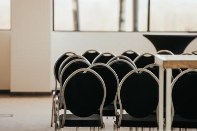 Rangées de chaises noires alignées dans une salle lumineuse avec une table en bois au premier plan.