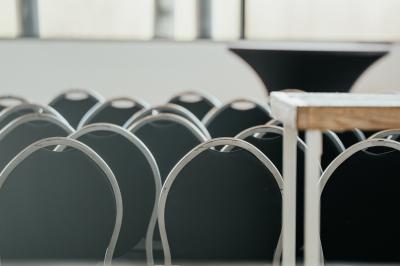 Rangées de chaises noires alignées dans une salle lumineuse avec une table en bois au premier plan.
