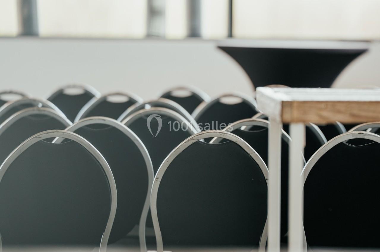 Rangées de chaises noires alignées dans une salle lumineuse avec une table en bois au premier plan.