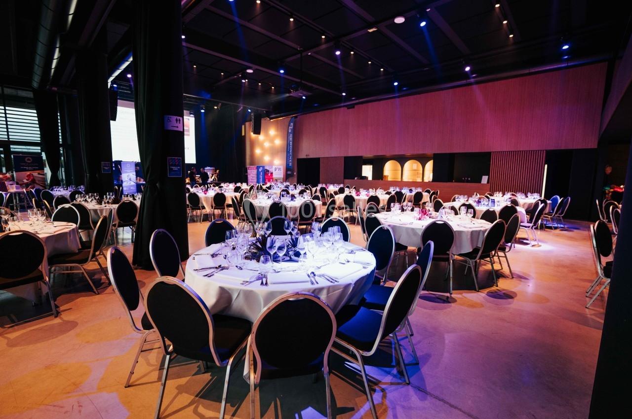 Salle de réception avec tables rondes dressées, nappes blanches et éclairage tamisé.