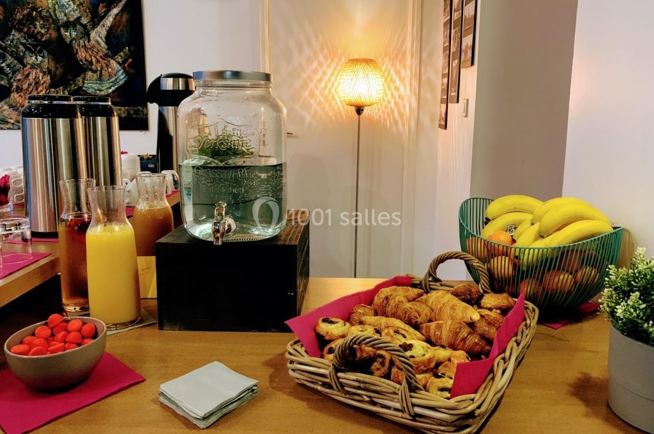 Table avec carafe d'eau, jus de fruits, viennoiseries, corbeille de fruits et éléments de décoration.