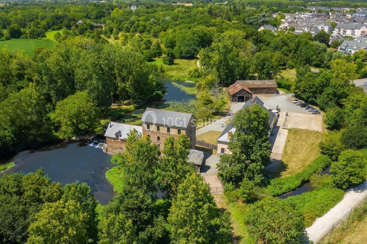Vue aérienne d'un moulin en pierre entouré de verdure, avec une rivière et des bâtiments annexes à proximité.