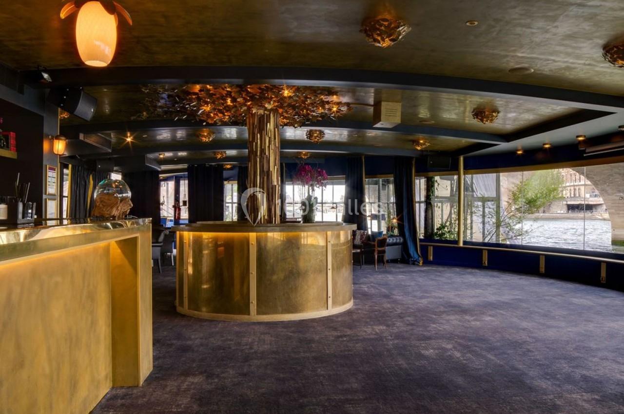 Intérieur d'un espace élégant avec bar doré, plafond décoré et grandes fenêtres donnant sur un paysage extérieur.