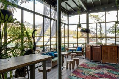 Bâtiment flottant moderne avec façade végétalisée, accessible par une passerelle en bois, amarré le long d'un quai pavé.