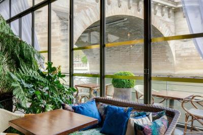 Bâtiment flottant moderne avec façade végétalisée, accessible par une passerelle en bois, amarré le long d'un quai pavé.