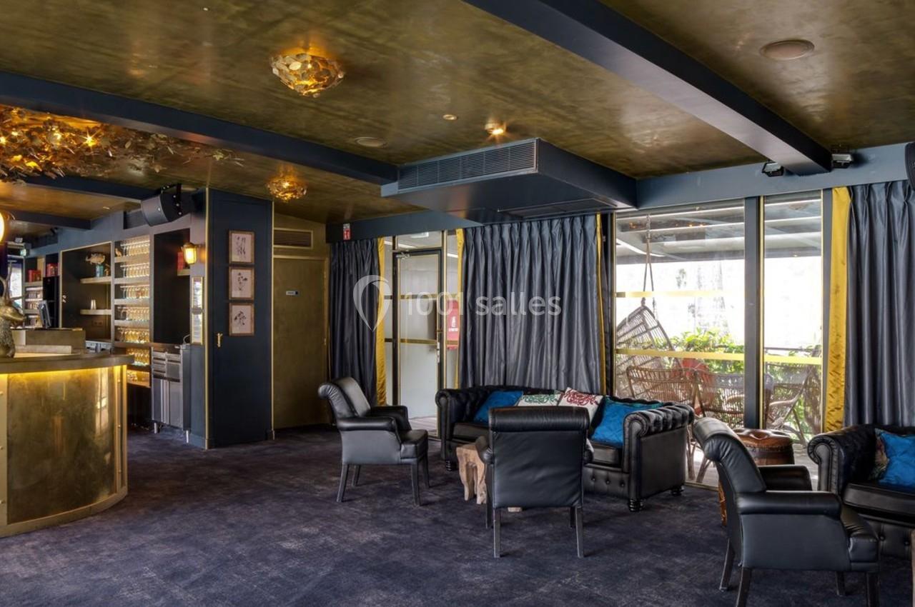 Salon élégant avec fauteuils en cuir, bar doré, rideaux sombres et grandes fenêtres donnant sur une terrasse.