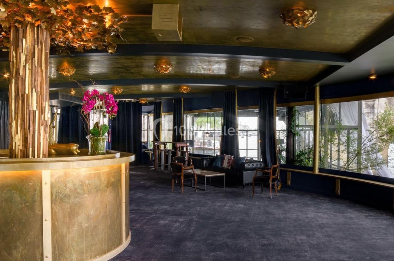 Intérieur d'un espace élégant avec un comptoir doré, des orchidées et de grandes baies vitrées donnant sur l'extérieur.