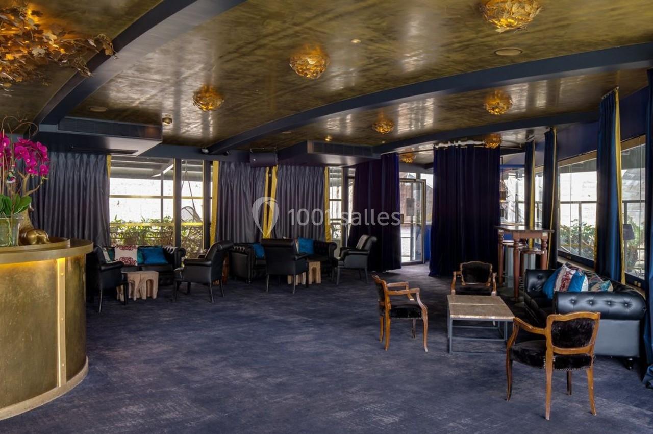 Intérieur d'un salon élégant avec des fauteuils, des tables basses, un comptoir doré et une décoration raffinée.