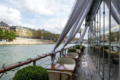 Bâtiment flottant moderne avec façade végétalisée, accessible par une passerelle en bois, amarré le long d'un quai pavé.