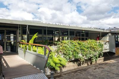 Bâtiment flottant moderne avec façade végétalisée, accessible par une passerelle en bois, amarré le long d'un quai pavé.
