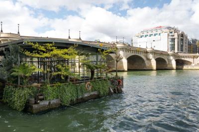 Bâtiment flottant moderne avec façade végétalisée, accessible par une passerelle en bois, amarré le long d'un quai pavé.