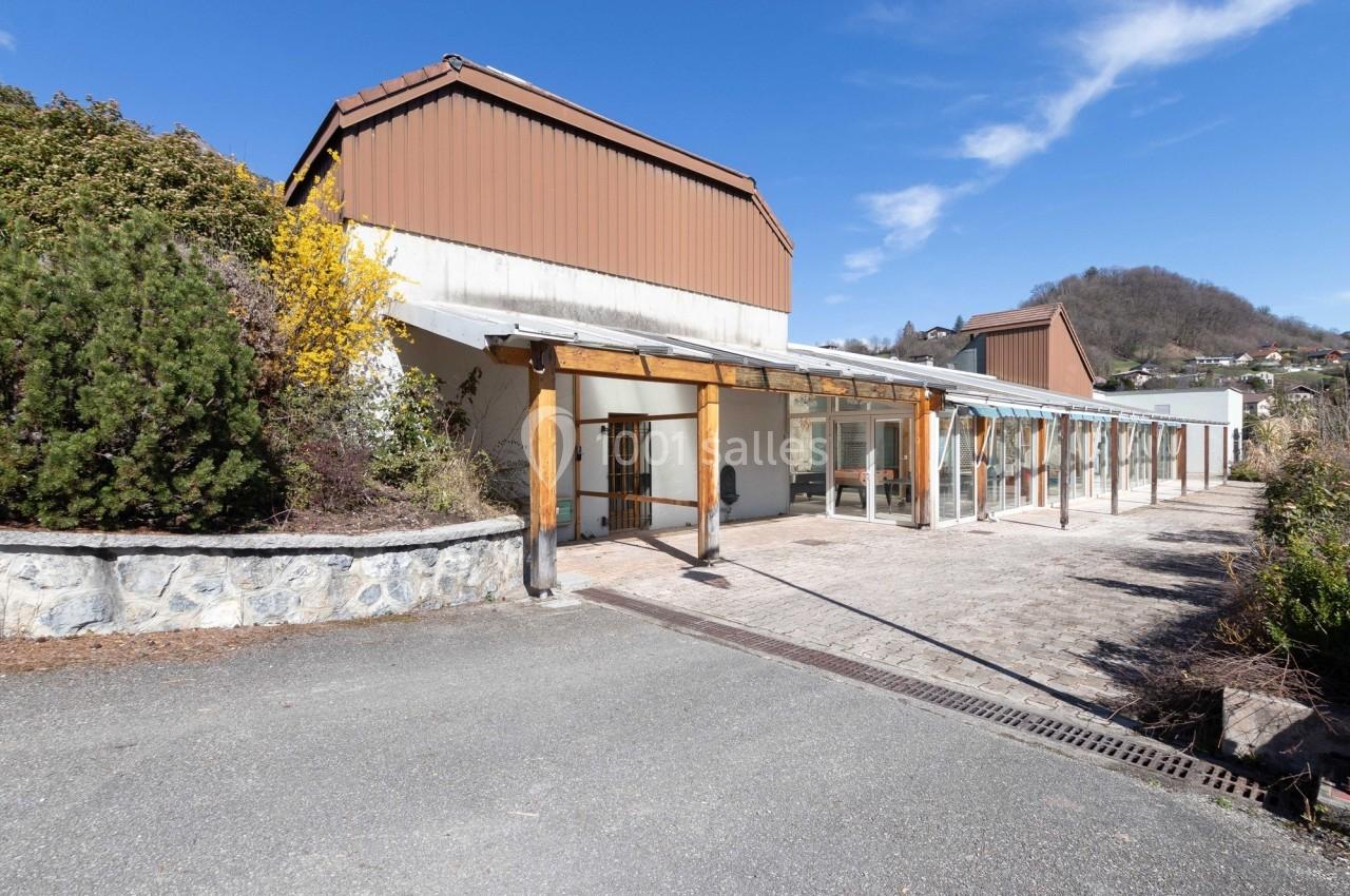 Bâtiment avec toit en pente, façade en verre et bois, entouré de végétation, sous un ciel bleu dégagé.