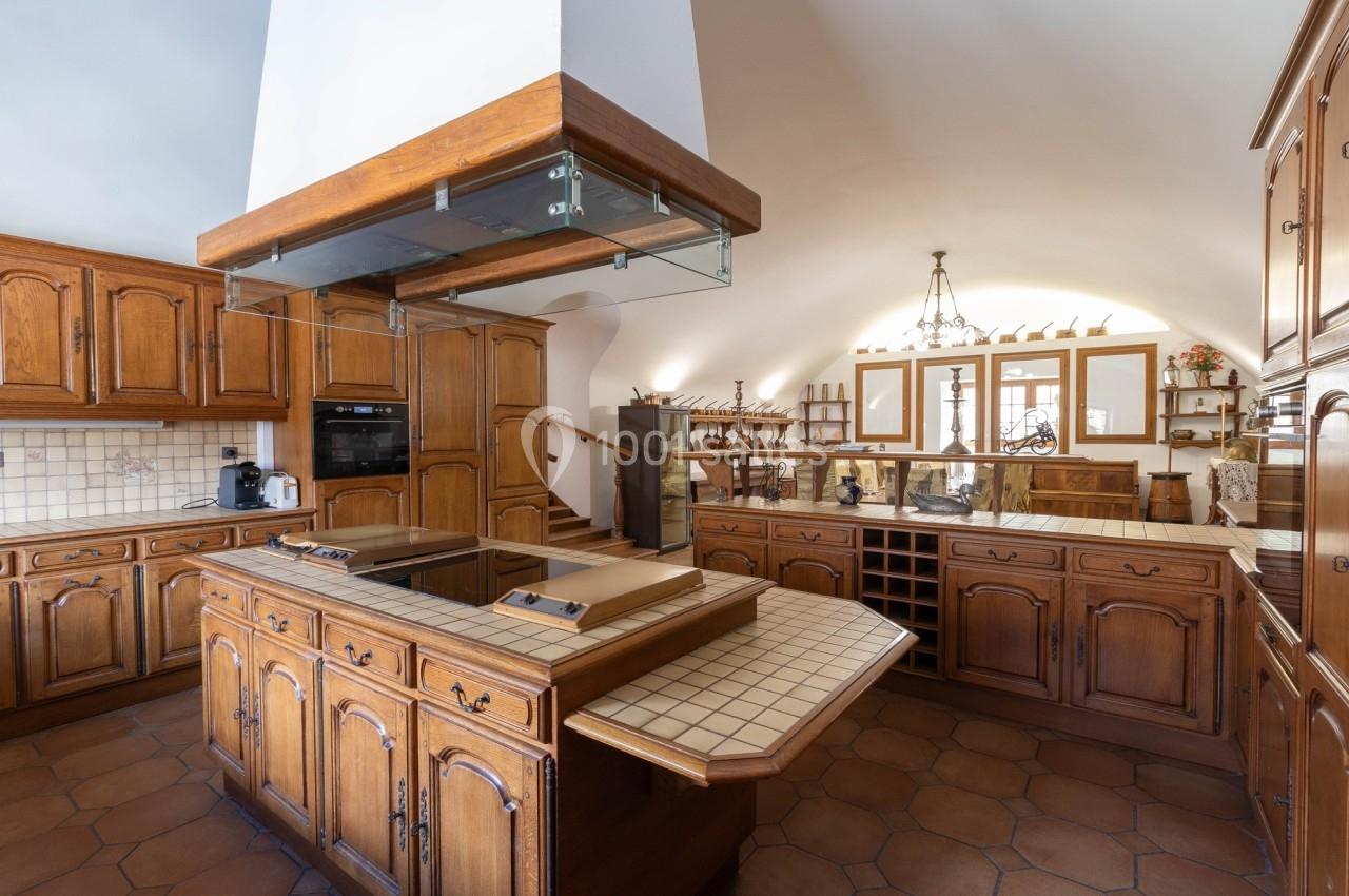 Cuisine spacieuse avec meubles en bois, îlot central carrelé, hotte suspendue et éclairage naturel.