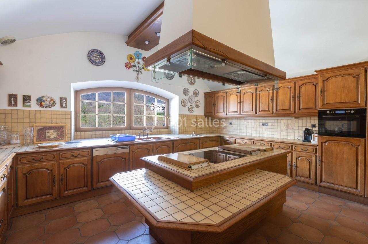 Cuisine traditionnelle avec meubles en bois, plan de travail carrelé, hotte centrale et fenêtre donnant sur l'extérieur.