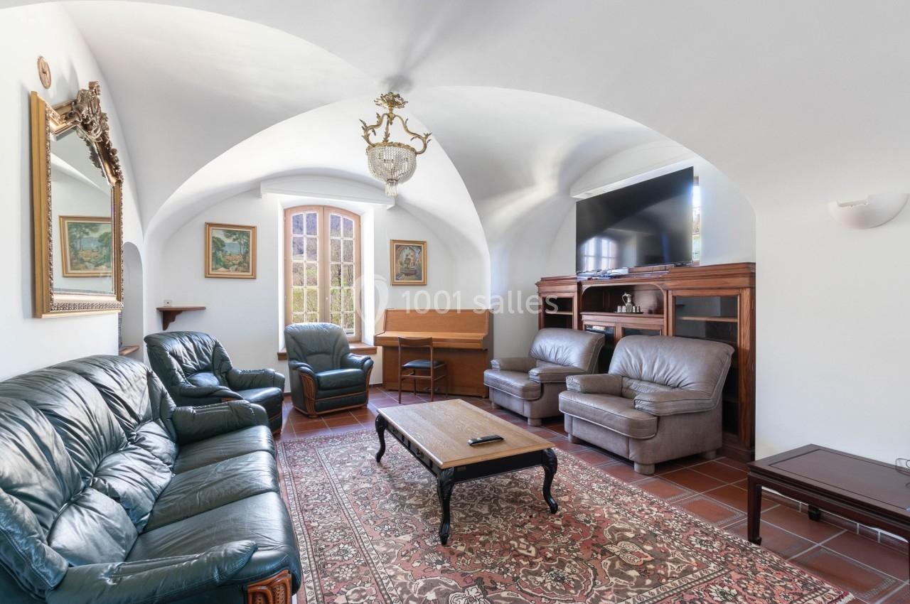 Salon lumineux avec plafond voûté, mobilier en cuir, tapis oriental, bureau en bois et grande télévision murale.