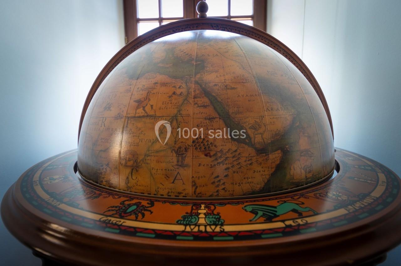 Globe terrestre ancien en bois et métal, montrant des cartes détaillées, placé devant une fenêtre lumineuse.