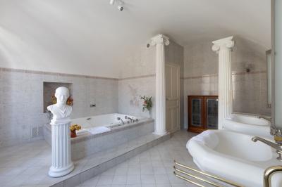 Salle de bain lumineuse avec baignoire, colonnes décoratives, miroir mural et carrelage clair.
