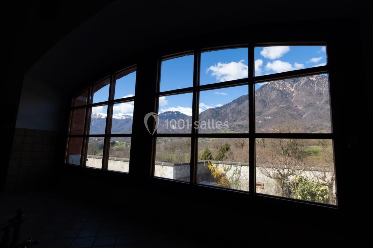 Vue sur des montagnes et un paysage rural à travers une grande fenêtre à carreaux.