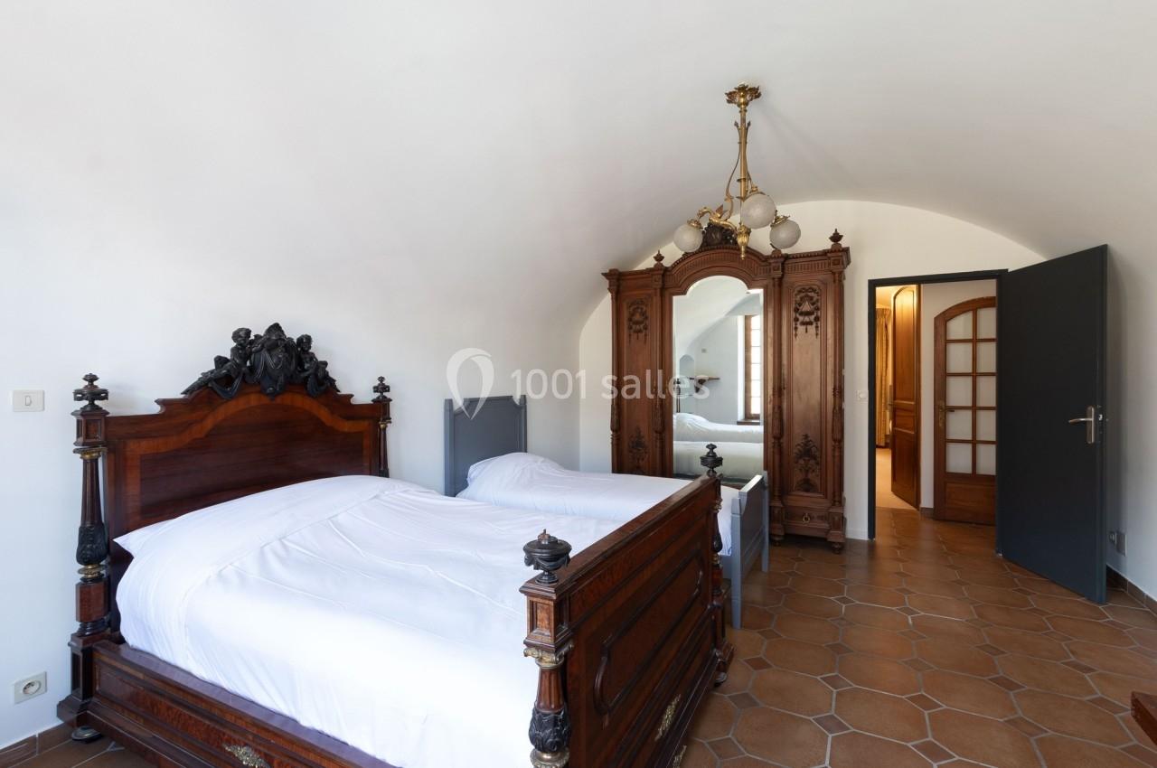 Chambre avec lit ancien en bois sculpté, armoire assortie, sol en carrelage et porte ouverte sur une autre pièce.