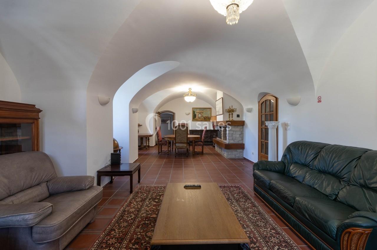 Salon spacieux avec voûtes blanches, meubles en bois, canapés, tapis rouge et cheminée en arrière-plan.