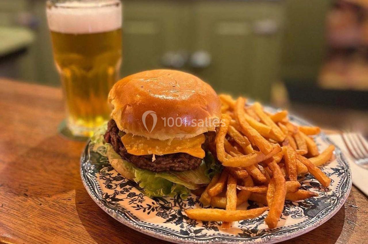 Burger au fromage avec laitue, servi avec des frites sur une assiette décorée, accompagné d'un verre de bière.