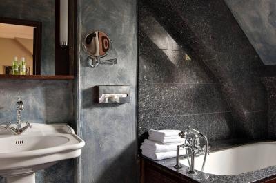 Salle de bain avec lavabo, miroir, baignoire en angle, serviettes pliées et murs en carrelage sombre.