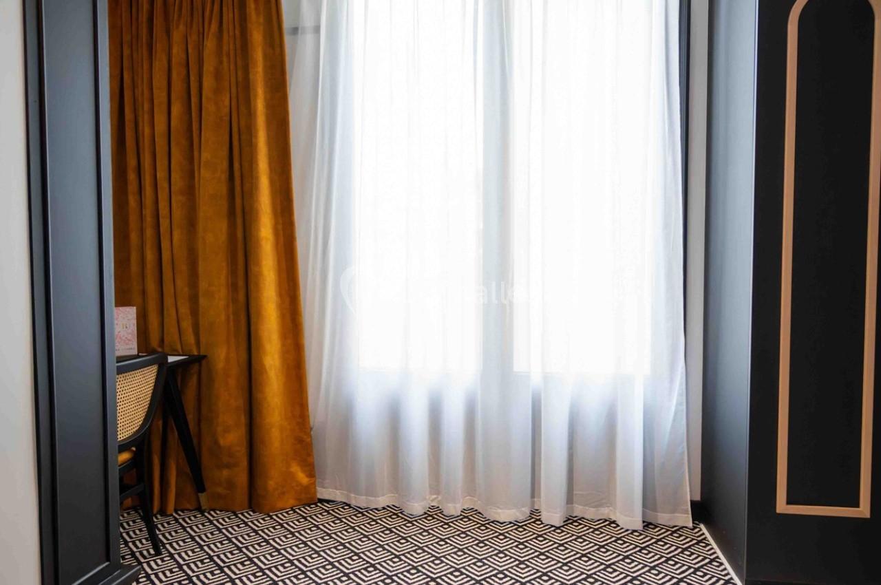 Rideaux dorés et voilages blancs encadrant une fenêtre, avec un tapis à motifs géométriques noir et blanc au sol.