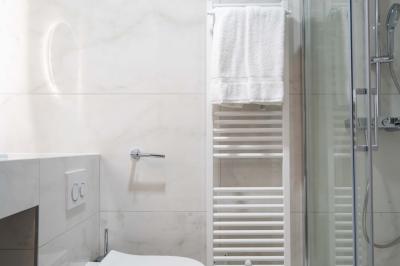 Salle de bain moderne avec toilettes suspendues, sèche-serviettes mural, douche vitrée et murs en carrelage clair.