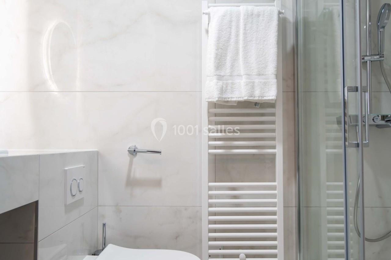 Salle de bain moderne avec toilettes suspendues, sèche-serviettes mural, douche vitrée et murs en carrelage clair.