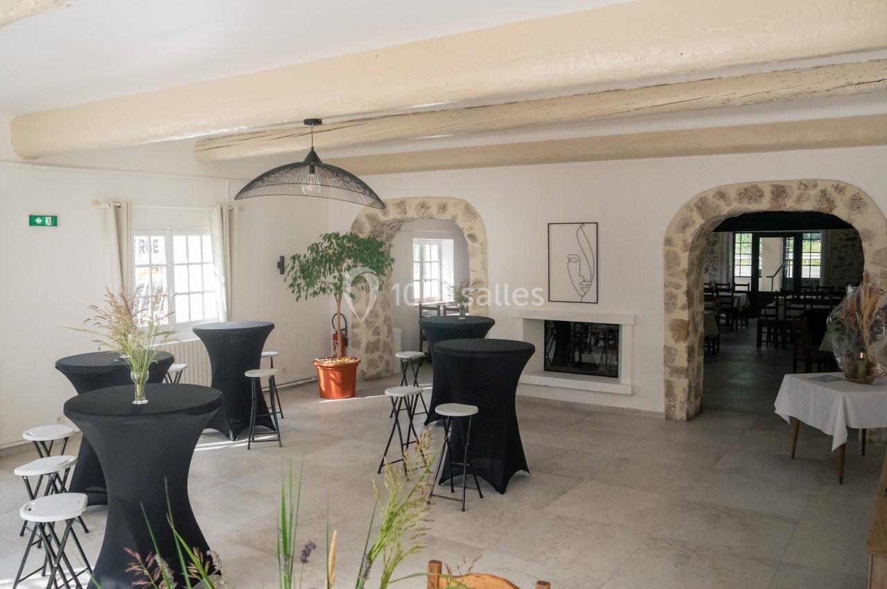 Salle lumineuse avec tables hautes noires, chaises, plantes et cheminée, décorée dans un style épuré et moderne.