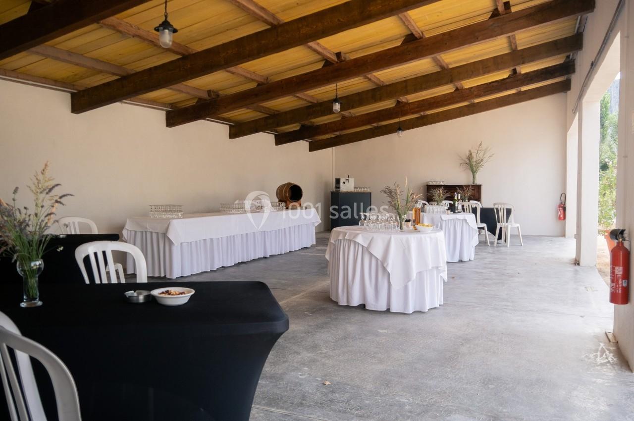 Salle avec tables dressées pour un événement, nappes blanches, chaises en plastique et décoration sobre.