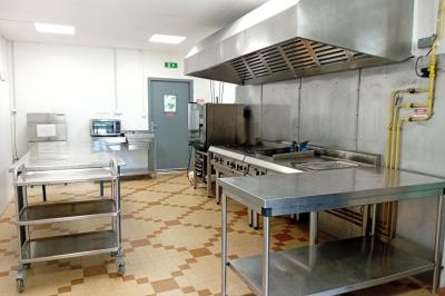 Cuisine professionnelle équipée avec plans de travail en inox, cuisinières, hotte et four à micro-ondes.