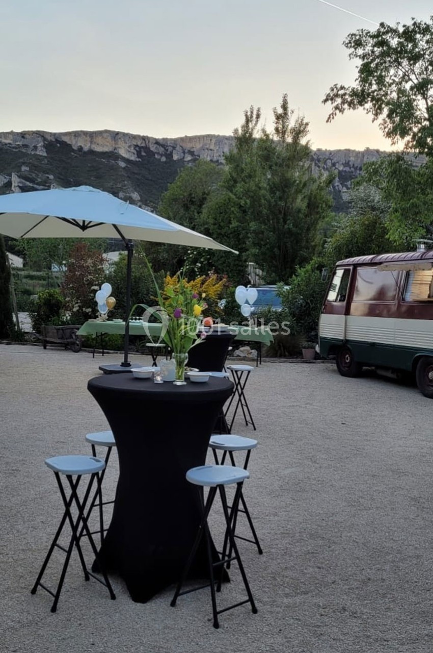 Table haute avec nappage noir, bouquet de fleurs, tabourets et parasol dans un espace extérieur avec vue sur des collines.