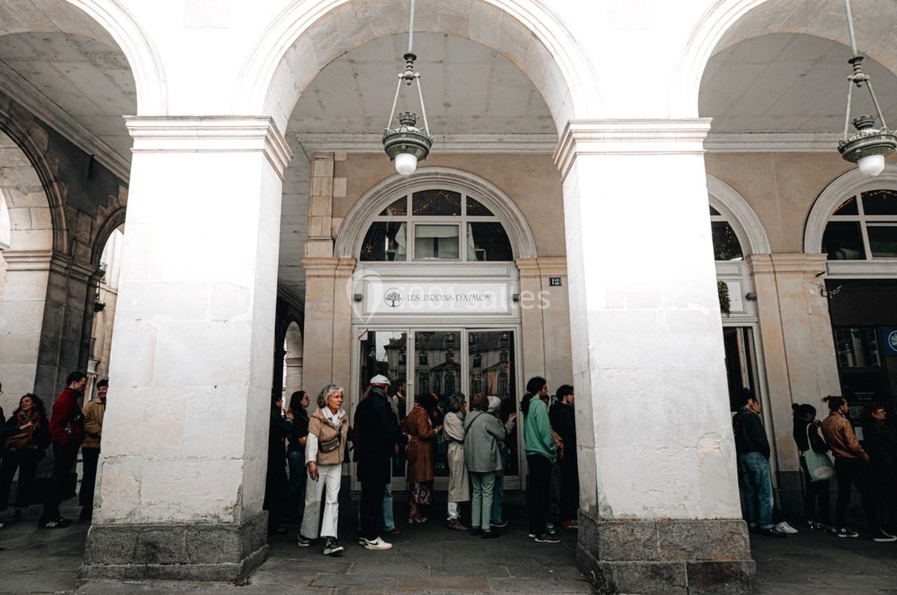 Des personnes font la queue sous des arcades devant l'entrée d'un bâtiment public ou commercial.