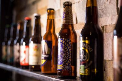 Bouteilles de bière variées alignées sur une étagère en bois devant un mur en pierre.