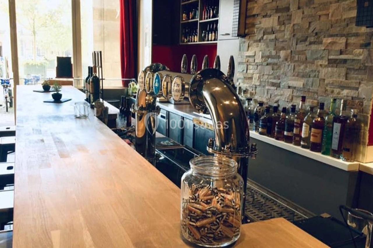 Comptoir de bar en bois avec tireuses à bière, bocaux et étagères de bouteilles en arrière-plan.