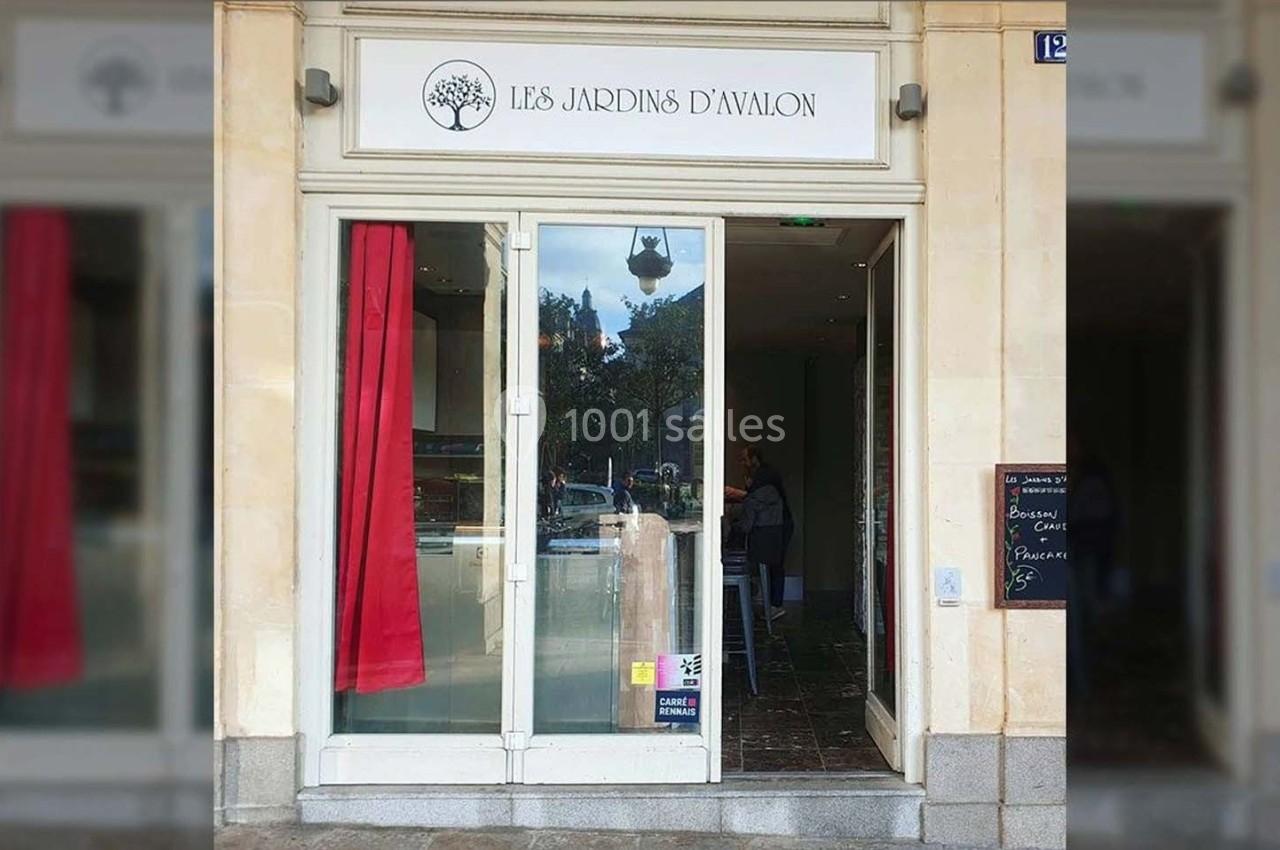 Façade d'une boutique avec une enseigne ’Les Jardins d'Avalon’, vitrine et porte en verre, rideaux rouges à l'intérieur.
