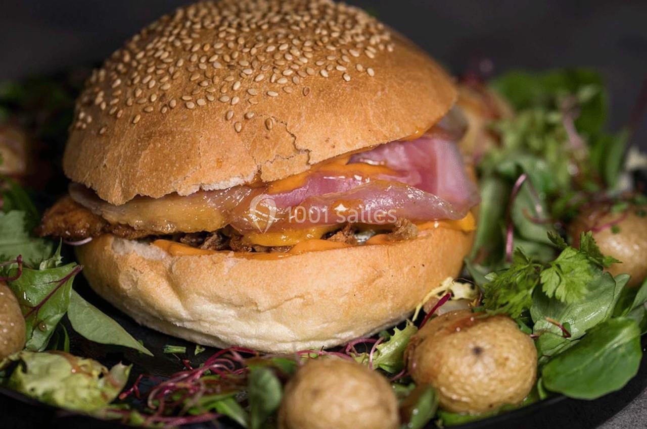 Burger garni de viande, fromage fondant et oignons, entouré de jeunes pousses et petites pommes de terre rôties.