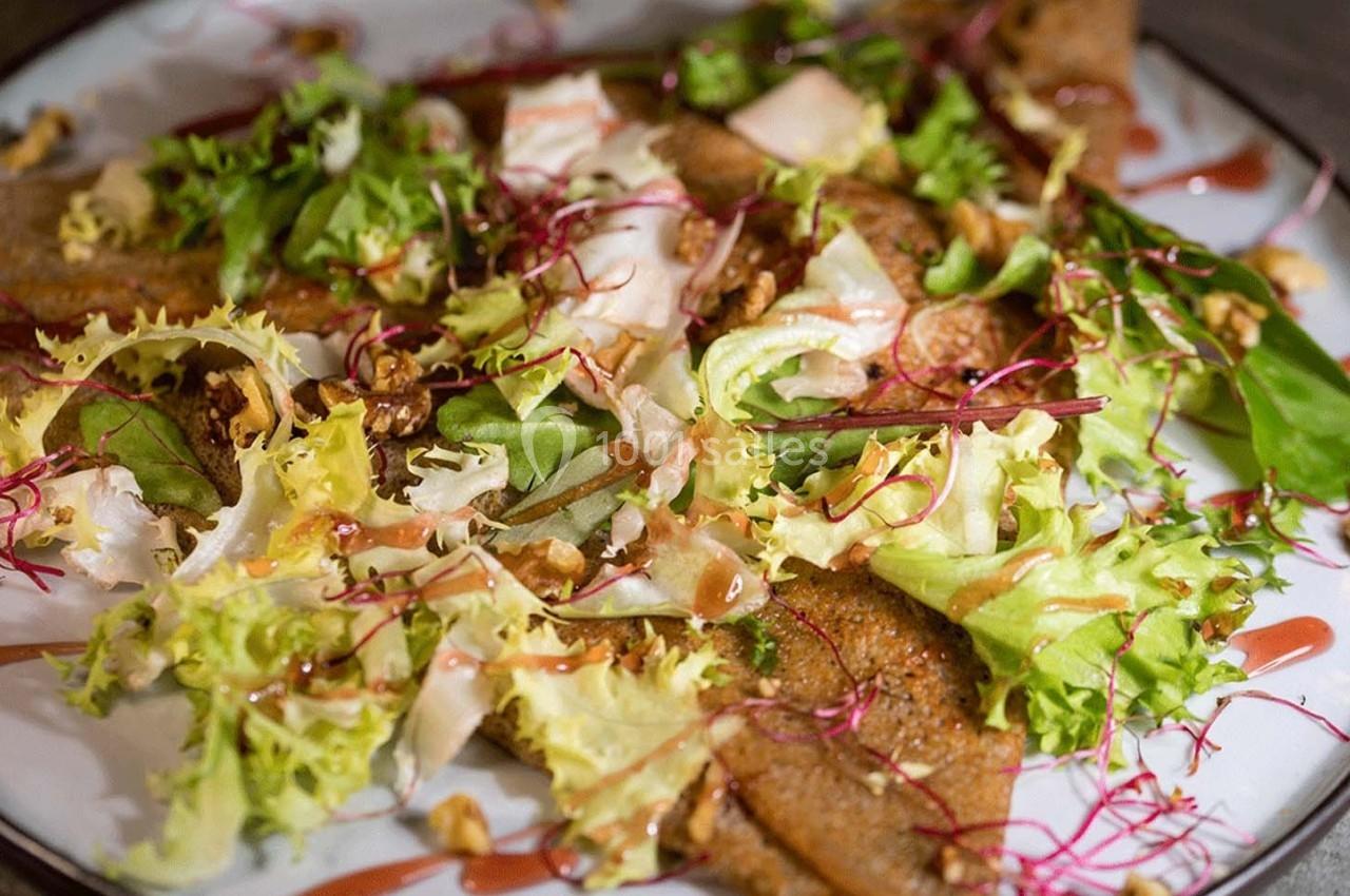 Assiette de galettes de sarrasin garnies de salade verte, pousses, noix et sauce.